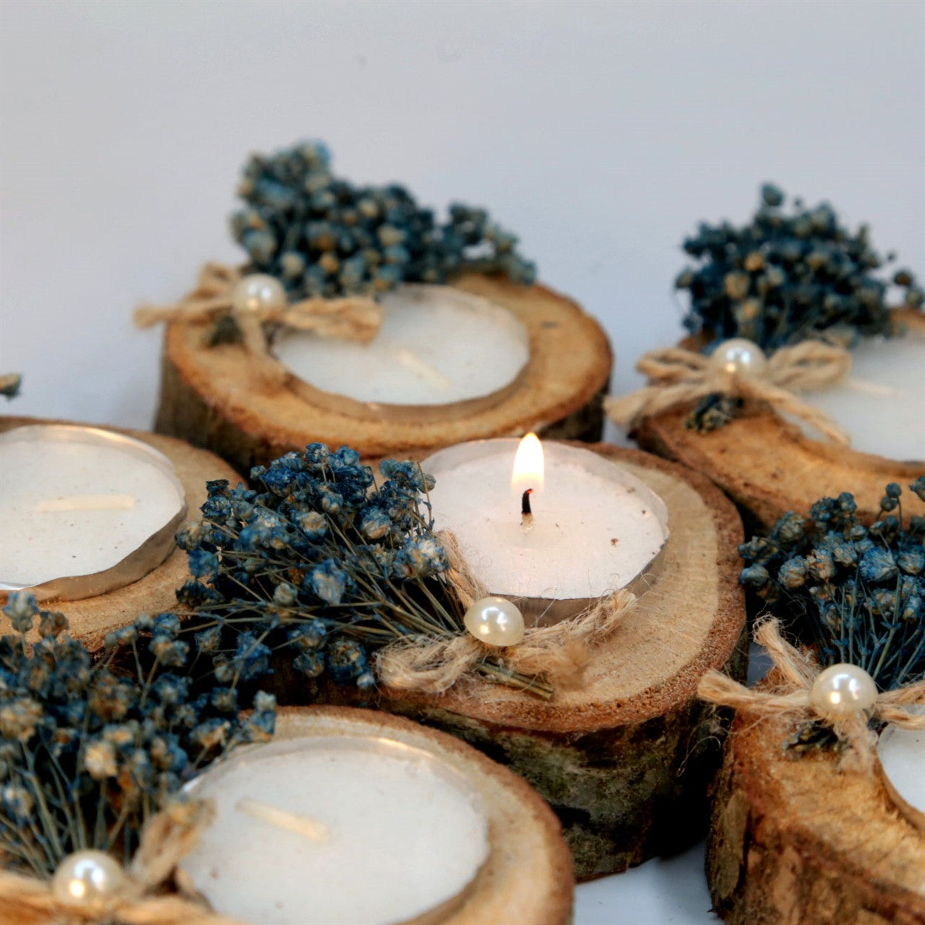 Rustikale Teelichtkerze in Holzscheibe mit blauen Trockenblumen und Perle