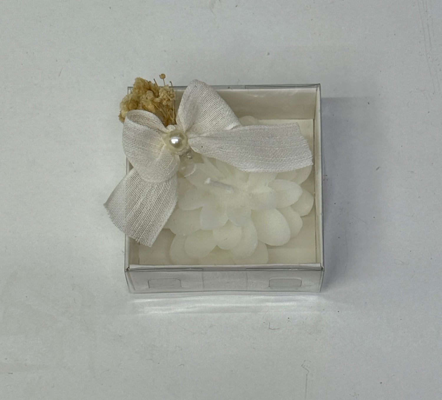 Weiße Blütenkerze in transparenter Box mit Schleife und Trockenblumen