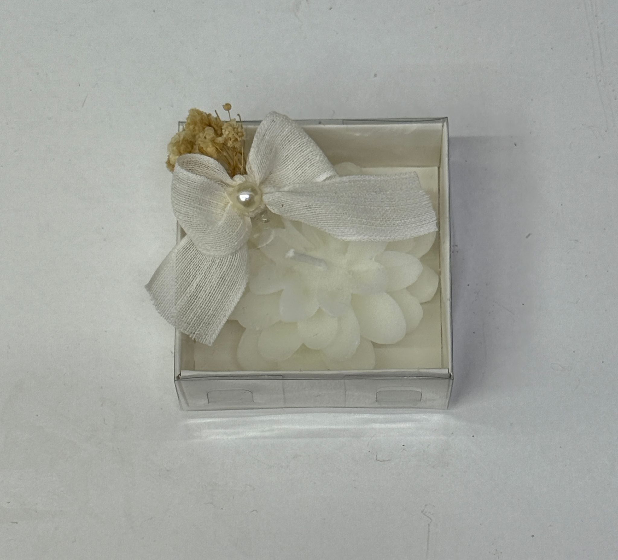 Weiße Blütenkerze in transparenter Box mit Schleife und Trockenblumen
