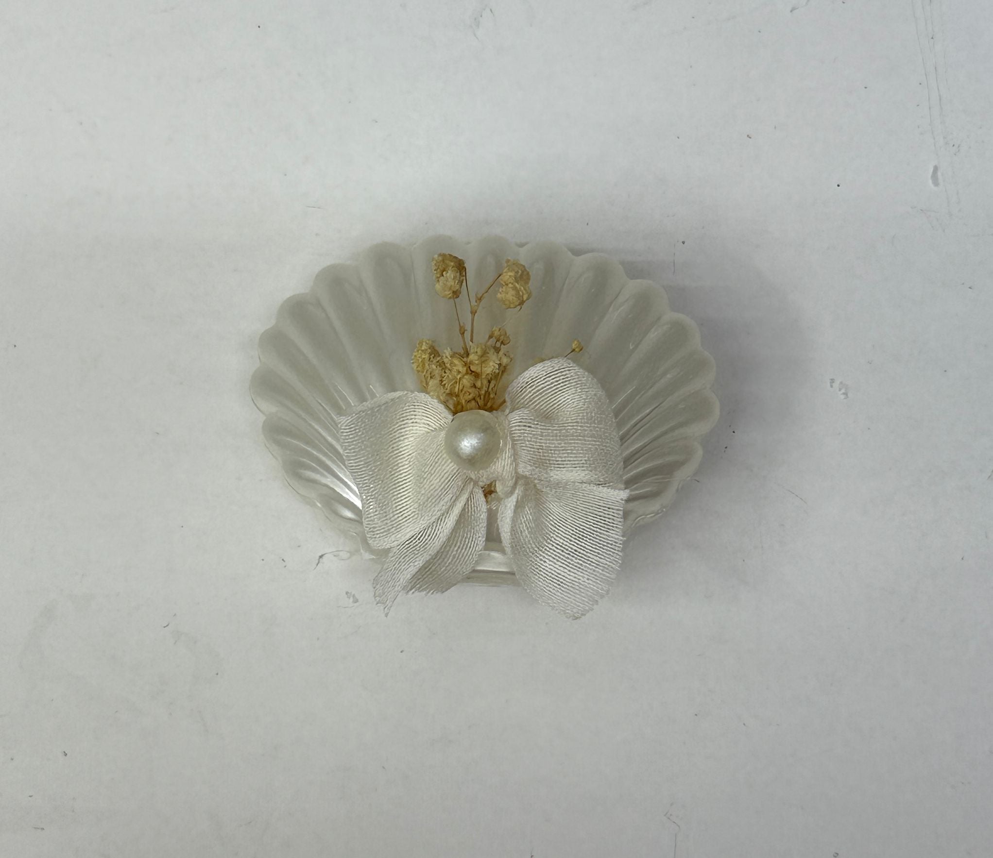 Weiße Kerze in Muschelform mit Schleife und Trockenblumen