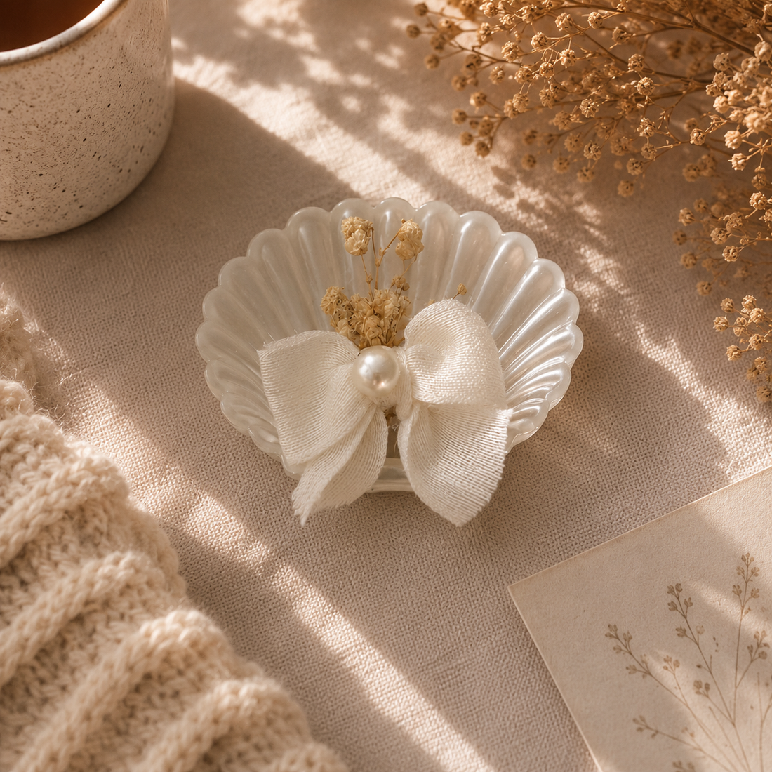 Weiße Kerze in Muschelform mit Schleife und Trockenblumen